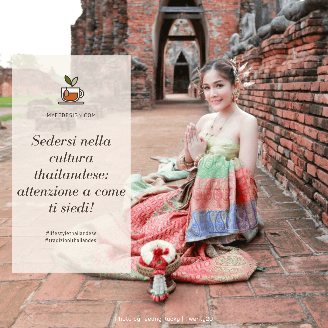 ragazza thailandese in costume tipico seduta per terra all'aperto, su un pavimento di mattoni con sulla destra un muretto anch'esso di mattoni e sullo sfondo degli archi che fanno pensare si trovi in un tempio buddista all'aperto