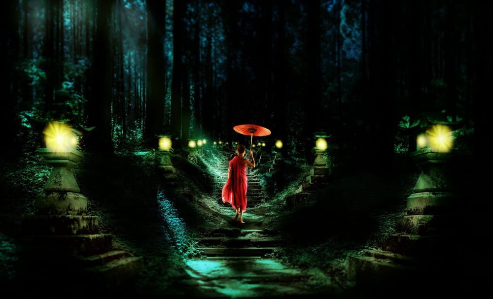 monaco buddista con ombrello che cammina in una foresta di notte