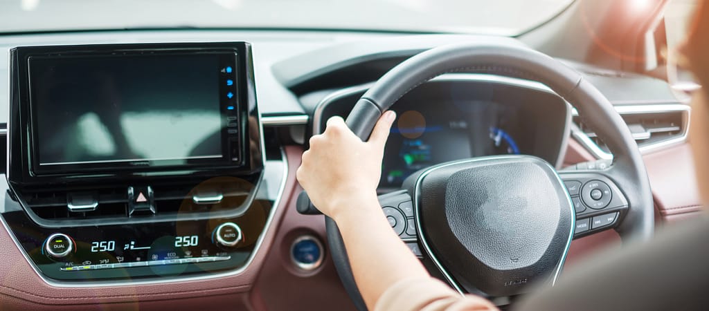 donna alla guida di un'auto su strada, volante controllato a mano in un'automobile elettrica moderna