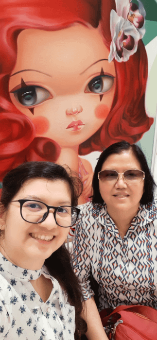ragazza e madre di fronte a un quadro surrealista pop con una ragazza dai capelli rossi e grandi occhi truccati con due linee verticali nere