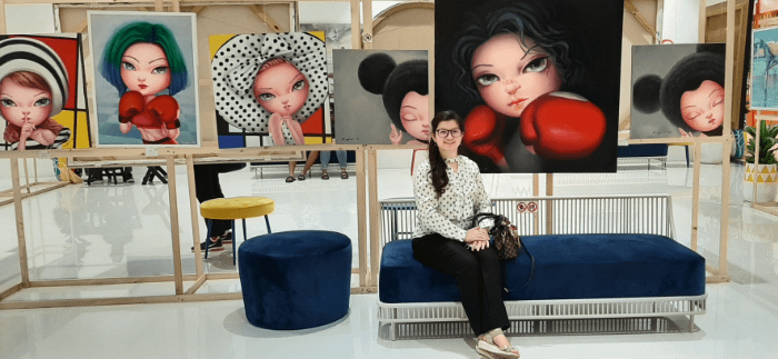 ragazza di fronte a diversi quadri in una esposizione artistica