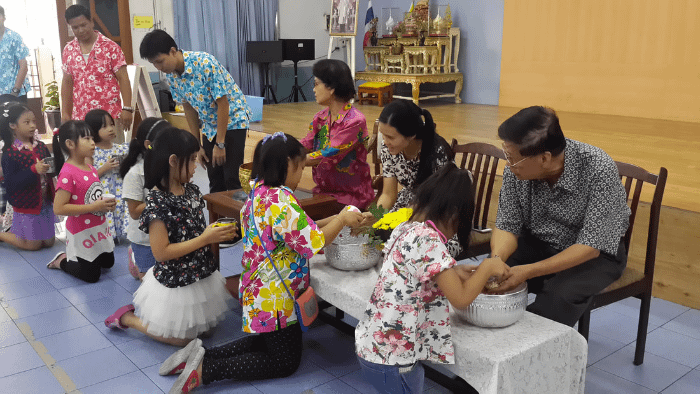 cerimonia thailandese del rod nam dam hua con tanti "anziani" seduti su delle sedie e i bambini inginocchiati a versare acqua sulle loro mani