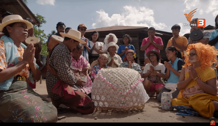 thailandesi inginocchiati a terra a pregare davanti ad una cesta in cui verrà posto un gatto da portare durante la processione per il rito per la pioggia