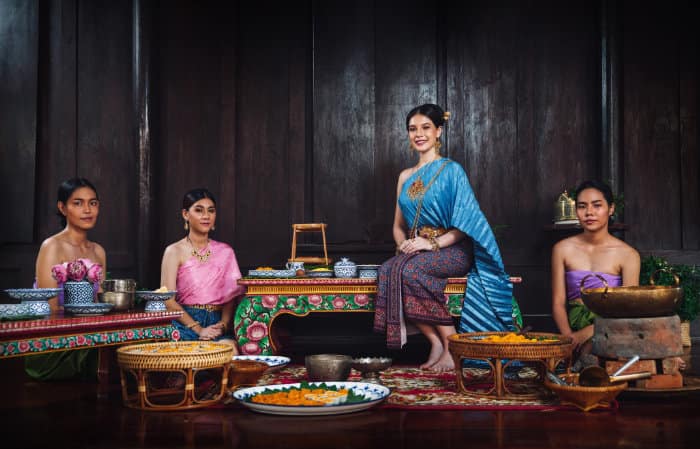 quattro donne thailandesi in costume tipico in una cucina tradizionale thailandese mentre preparano dei dolci