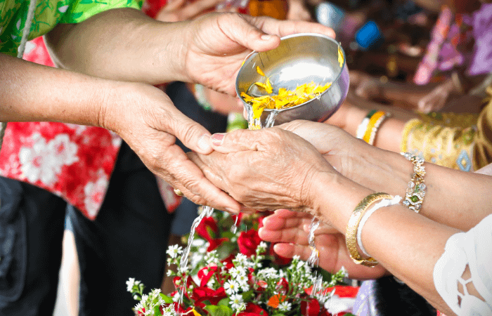 dettaglio di mani che vengono bagnate tramite una ciotola in acciaio, che contiene acqua profumata con petali di fiori. Si tratta di una cerimonia thailandese tipica per festeggiare il songkran, il capodanno thailandese che si celebra in aprile