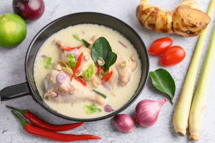 zuppa tom kha kai in un piatto circondato dagli ingredienti utilizzati per prepararlo