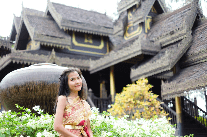 donna thailandese in abiti tradizionali di fronte a una casa tipica thailandese