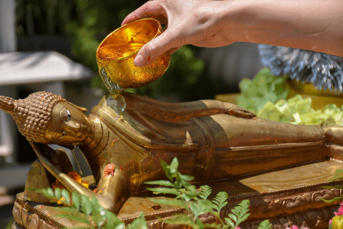 persona che versa l'acqua su una statua di Buddha tramite una ciotolina dorata