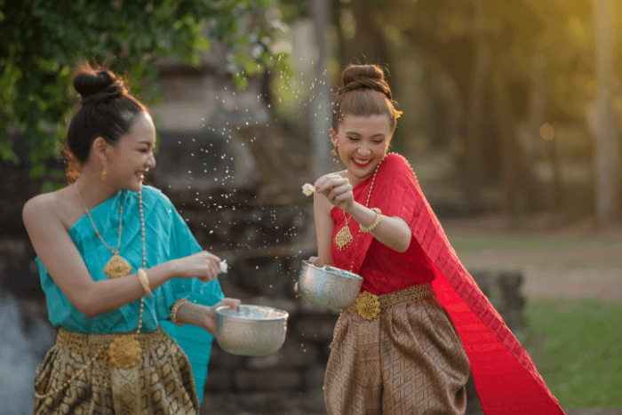 due donne thailandesi in costumi tipici con in mano una ciotola d'acqua in argento che si spruzzano acqua per il songkran, il capodanno thailandese