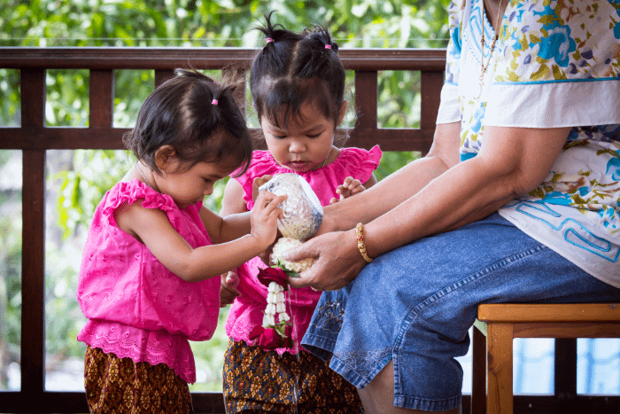 bambine thailandesi in costume tipico che offrono una ghirlanda di fiori ad una donna seduta per il songkran, il capodanno thailandese di aprile