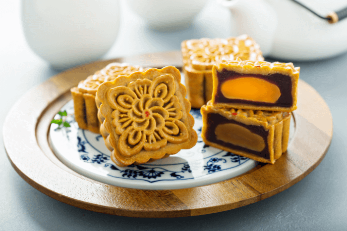 Piatto di Mooncake, con un dolcetto intero sulla sinistra, a forma di quadrato e con una complicata decorazione a forma di fiore sulla parte superiore, e un dolcetto tagliato a metà per mostrare il ripieno con il tuorlo d'uovo salato
