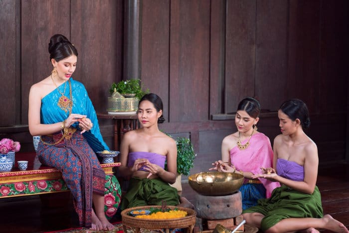 quattro donne thailandesi in costume tipico in una cucina tradizionale thailandese mentre preparano dei dolci