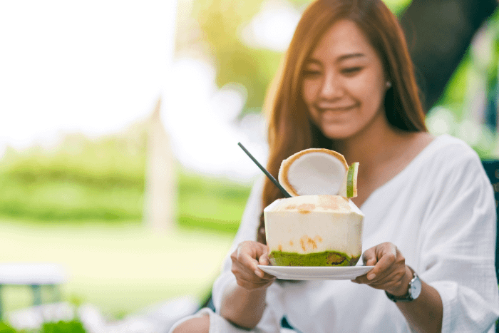 una donna thailandese con in mano un cocco aperto pronto da bere