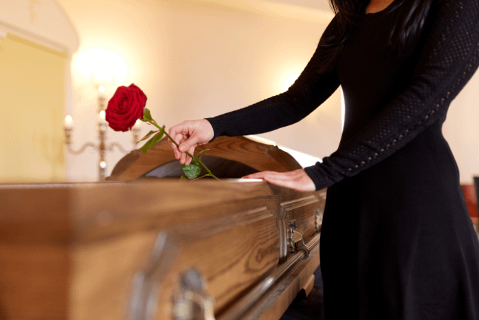 una donna vestita di nero accanto ad una bara con una rosa rossa in mano