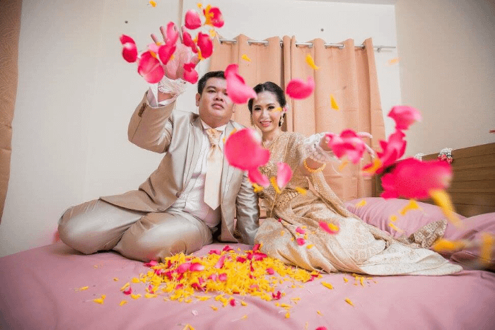 due neo sposi thailandesi che lanciano dei petali di rosa verso lo spettatore