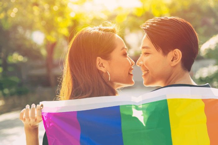 coppia LGBTQ+ thailandese che si sorridono abbracciati ad una bandiera arcobaleno