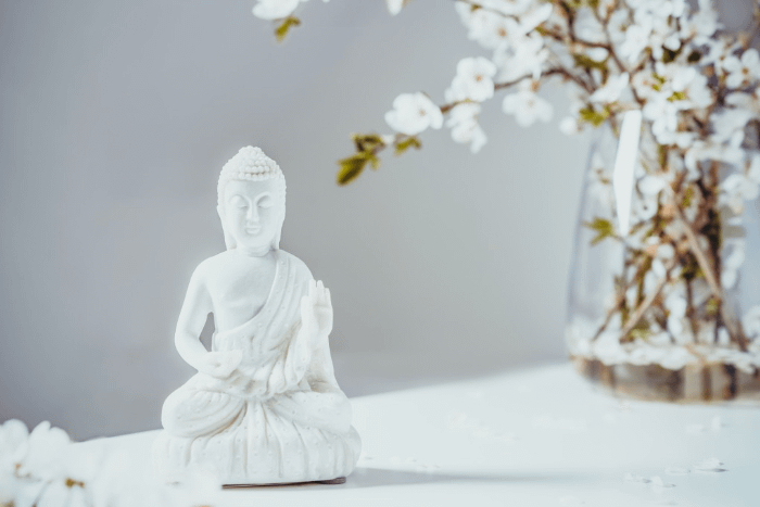 statua di buddha bianca con in sfondo un vaso di fiori bianco