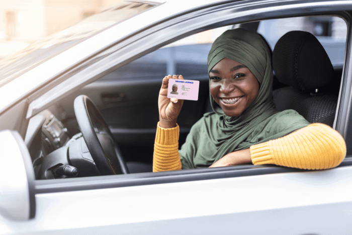 Donna di colore sorridente all'interno della sua automobile con patente in mano