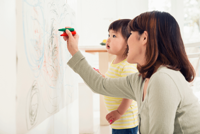 mamma e bimba asiatiche che disegnano su un foglio sul muro