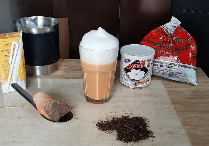 bicchiere di cha thai con attorno gli ingredienti necessari per prepararlo: il tè, il latte e il latte condensato