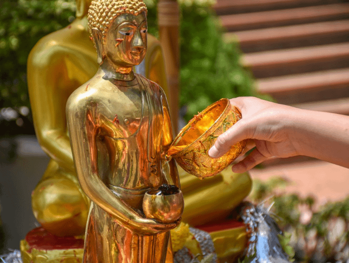 Persona che versa l'acqua presente in una ciotolina dorata su una statua di Buddha